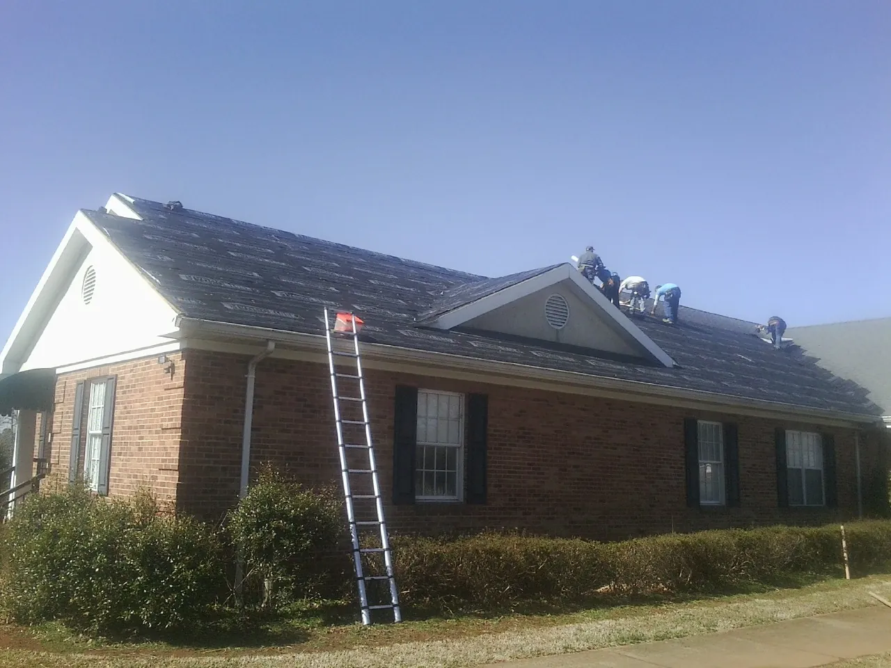 Crew tearing shingles off a brick ranch roof with a ladder set — Metal Roof Repair work by our crew in Ransomville