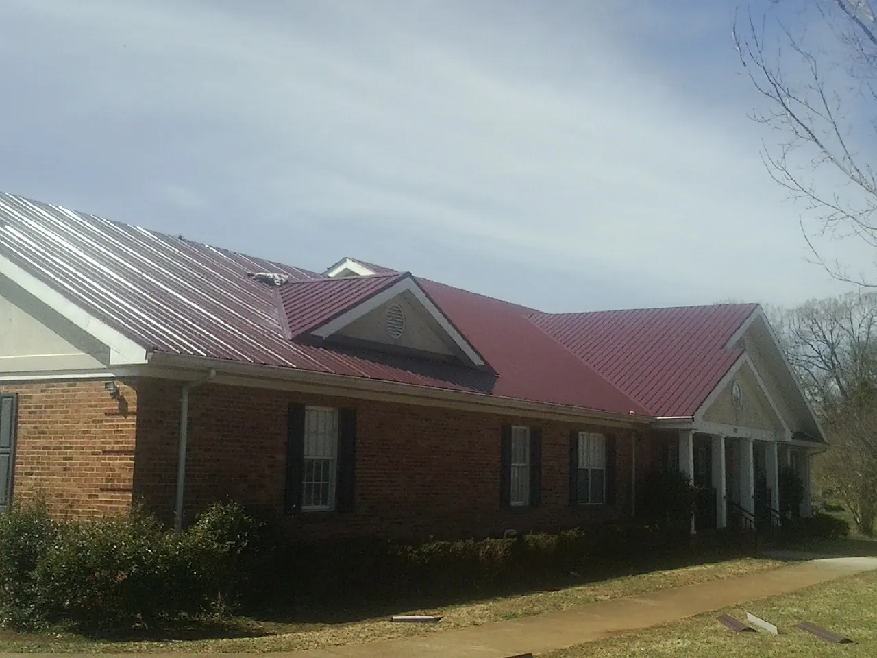 Red metal roof with gabled entries on a long brick building, from a Hail Damage Roof Repair job in Ransomville