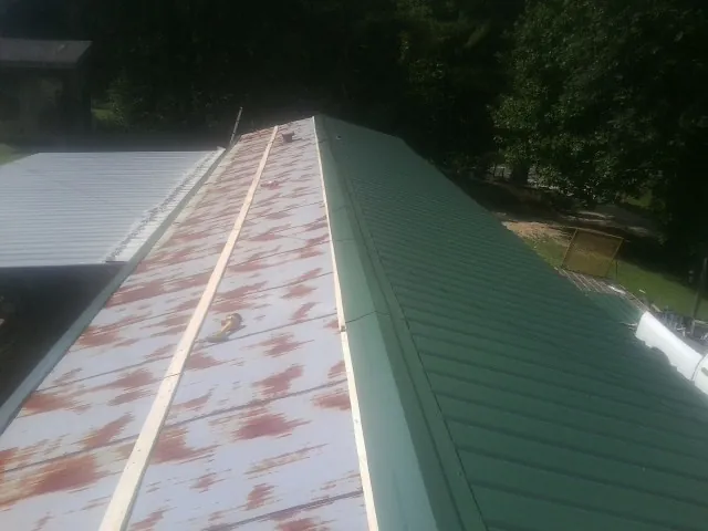 Old rusted panels beside newly installed green metal roofing — Wind Damage Roof Repair by Roofing Brothers in Ransomville