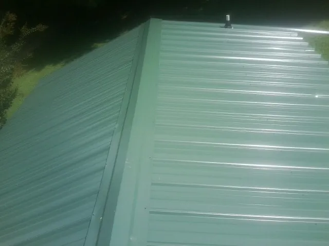 New green metal panels meeting at the ridge of a roof — Flat Roof Repair work by our crew in Ransomville