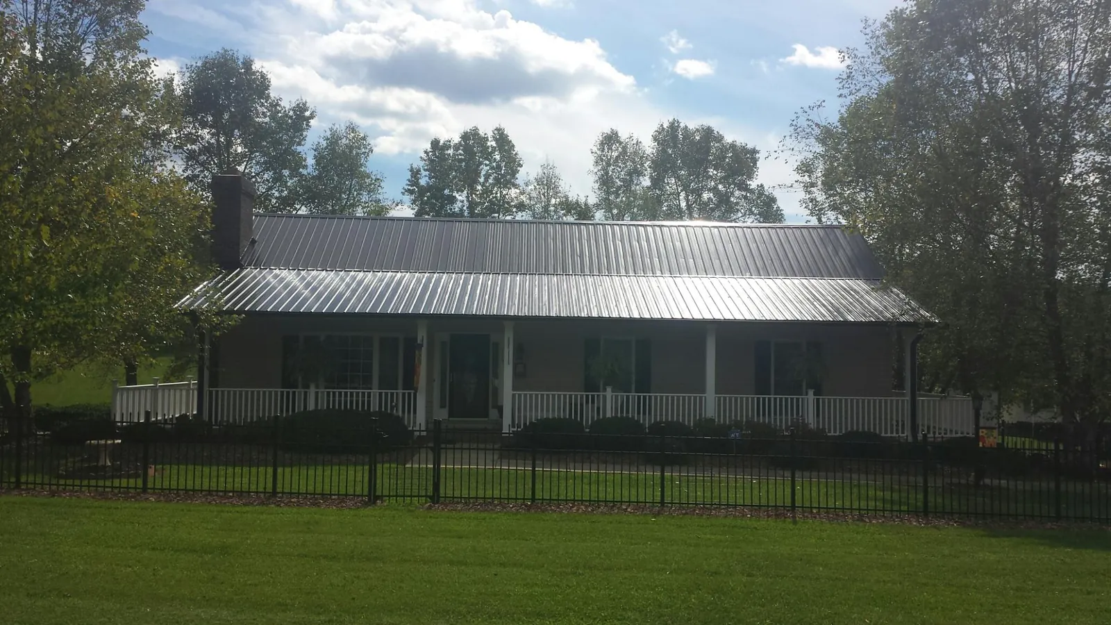 Gray metal roof on a brick ranch with a full width front porch — Gutter Guard Installation work by our crew in Ransomville