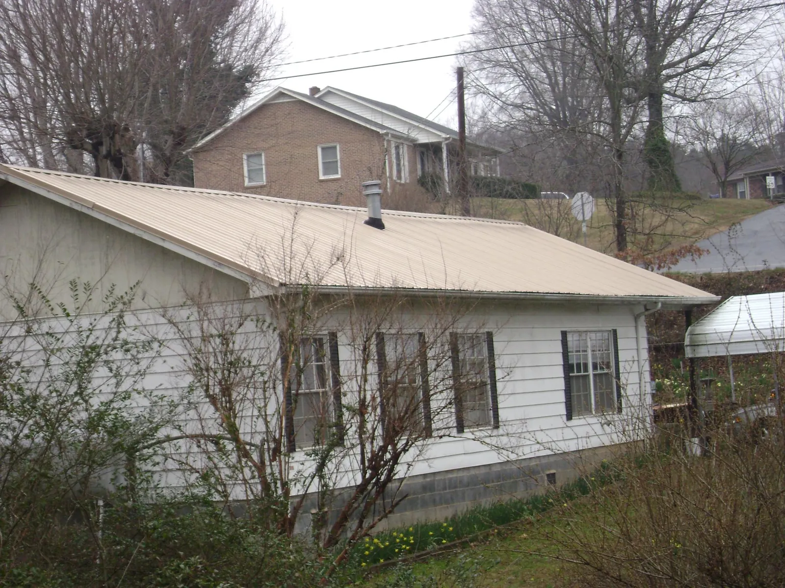 Tan metal roof on a white sided house set into a hillside — Commercial Roofing by Roofing Brothers in Ransomville