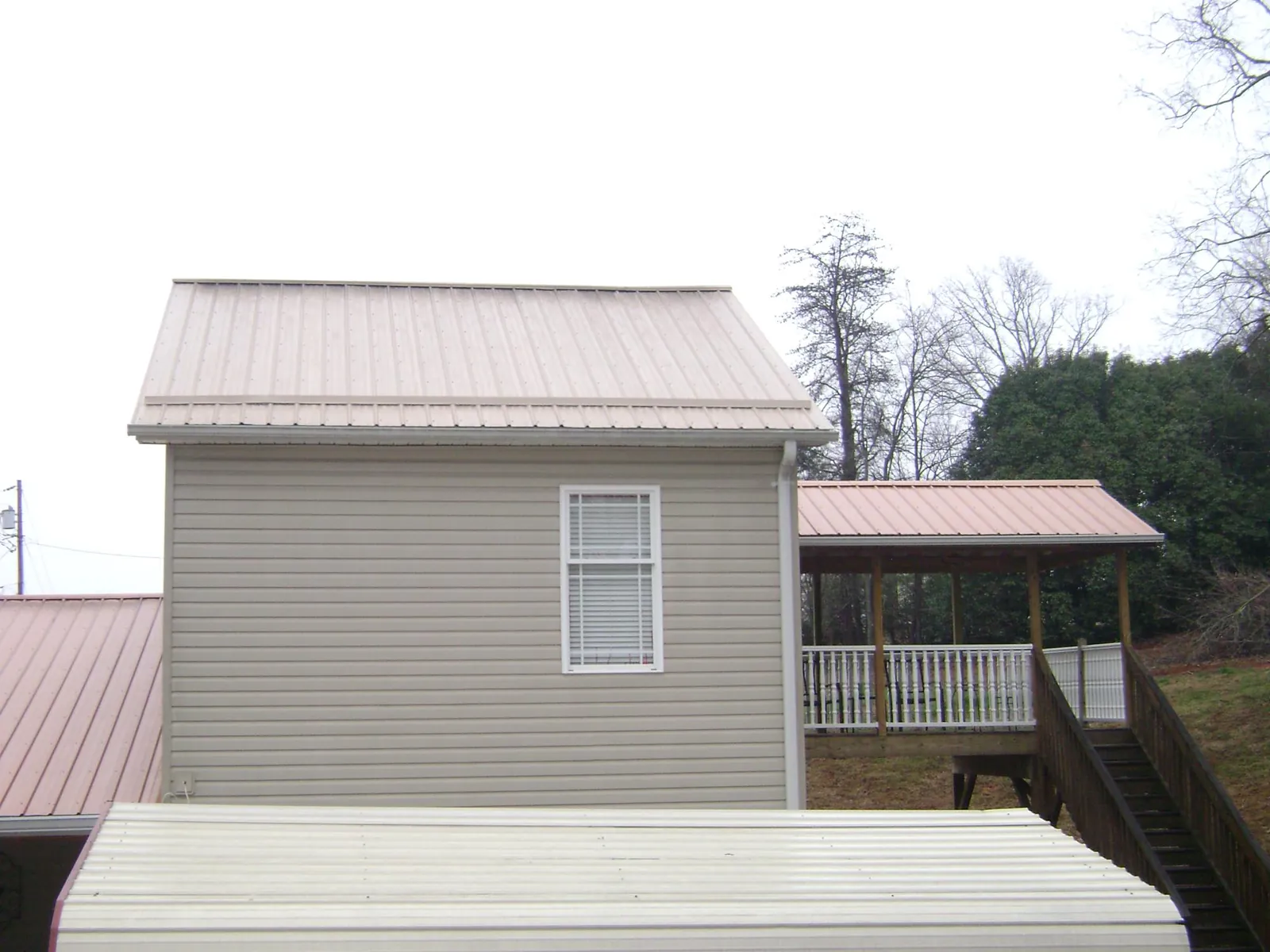 Tan metal roofs on a two story addition and attached porch, from a Roof Replacement job in Ransomville